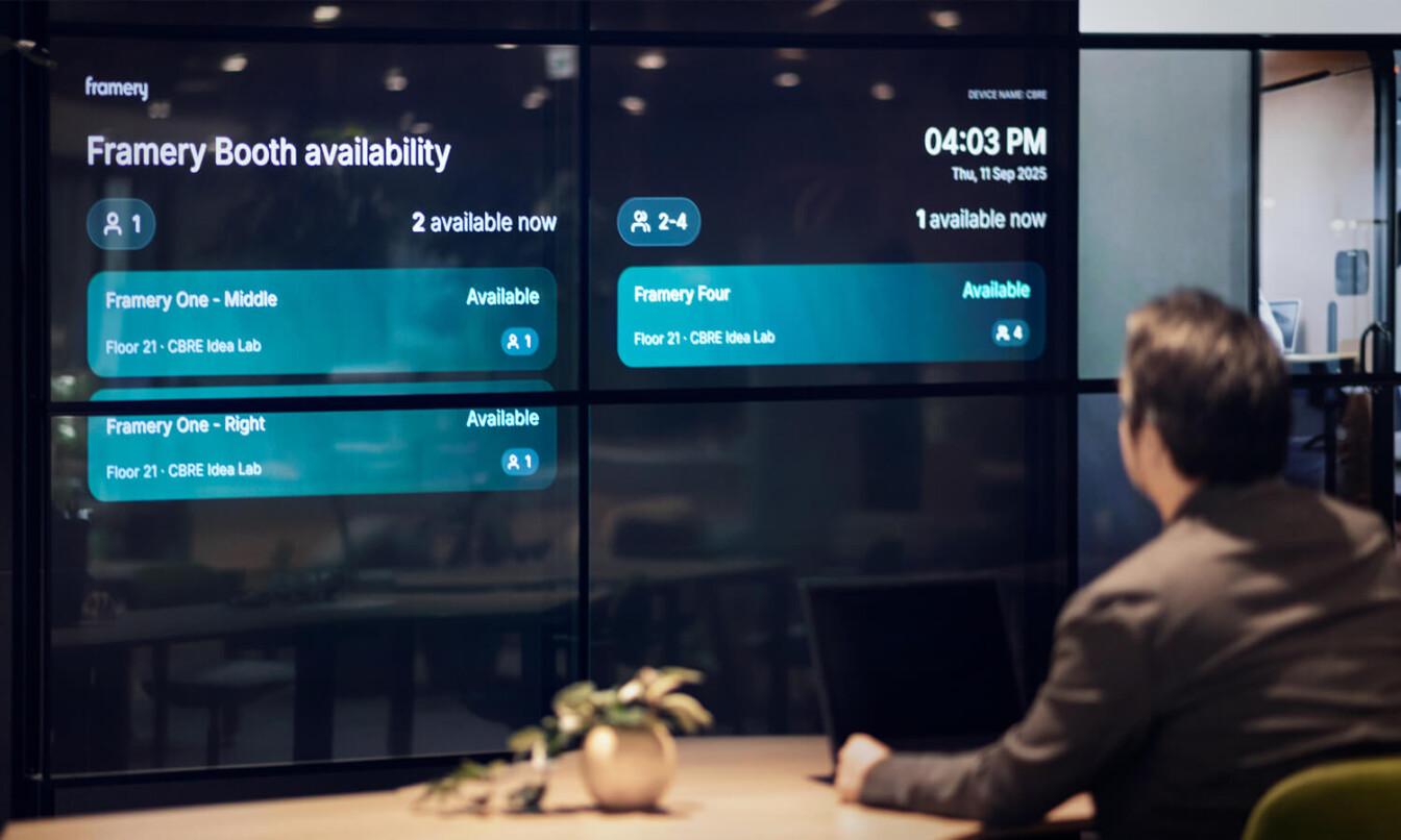 A person looks at a digital display showing Framery Space Overview in an office setting, with time and location details.