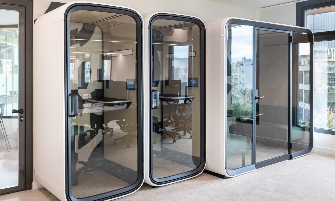 Modern office space with Framery soundproof pods for private meetings or phone calls, featuring chairs, desks, and large windows with city views.