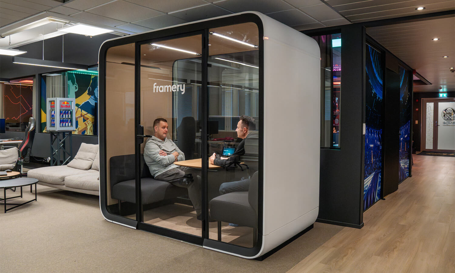 Two men sitting inside a white color Framery pod inside and office.