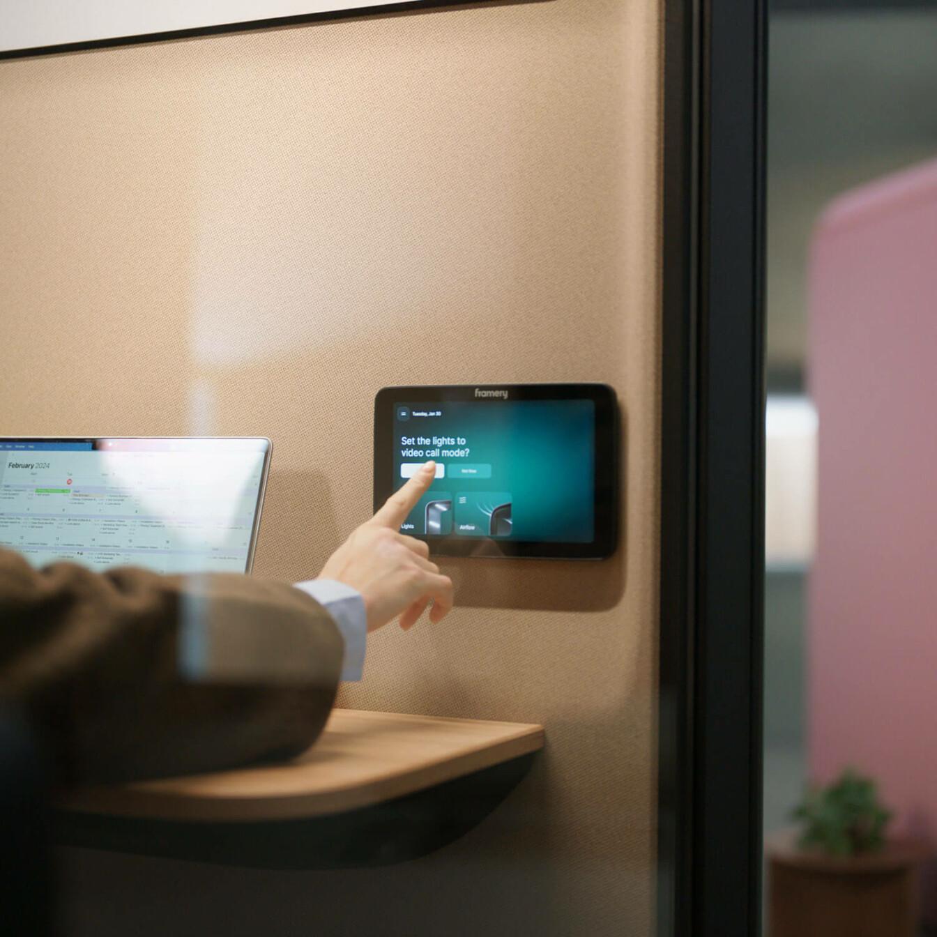A person pressing the "turn on" button on a touch screen inside a Framery One Compact office phone booth, to turn on the video call mode.