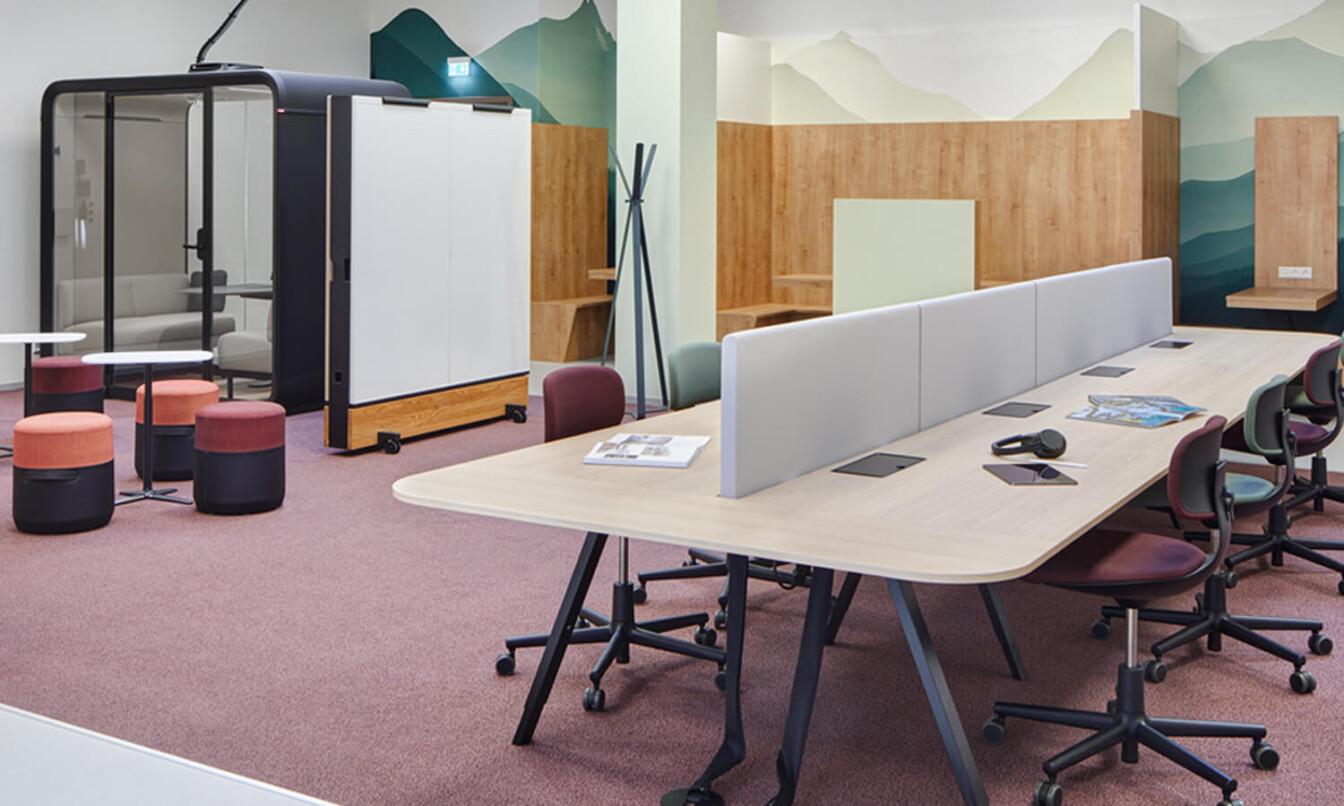 Modern classroom with shared desks, chairs, and a learning pod. Partition and vibrant decor enhance functionality and aesthetic.