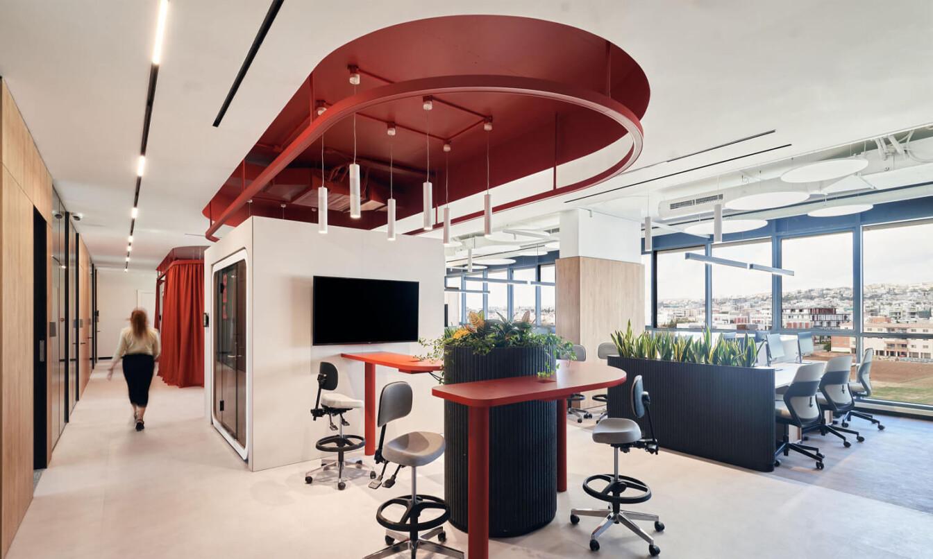 A light colored office with red details and office pods in the middle.