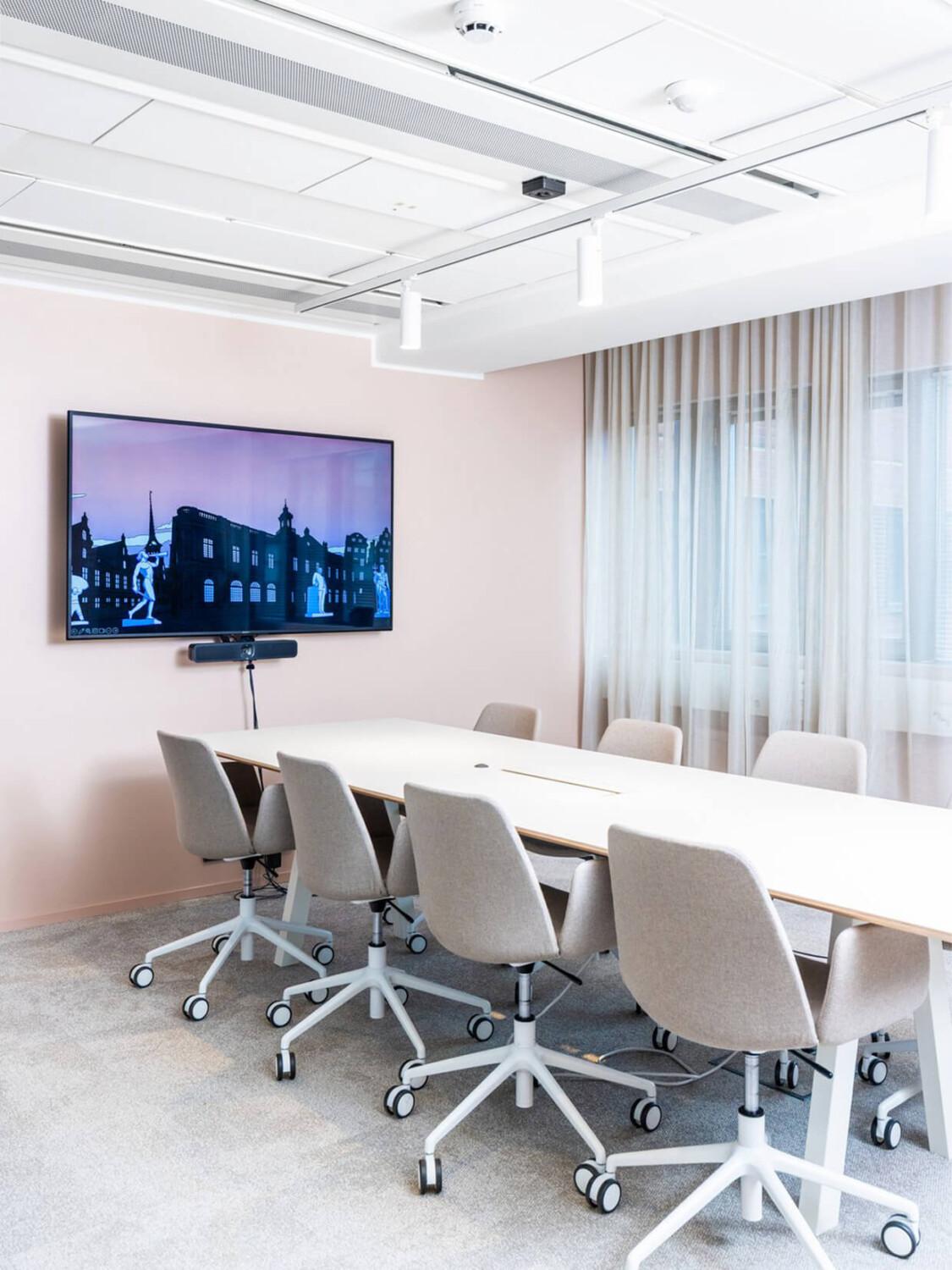 A light colored meeting room with long desk, chairs and TV screen.