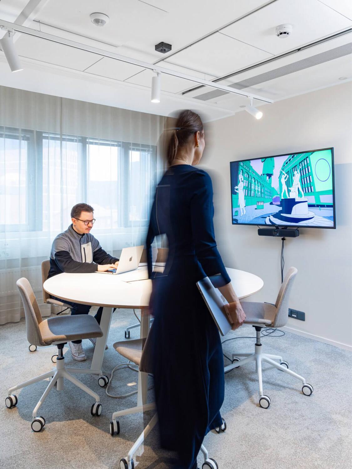 Woman walking into a meeting room with a man sitting by the table.