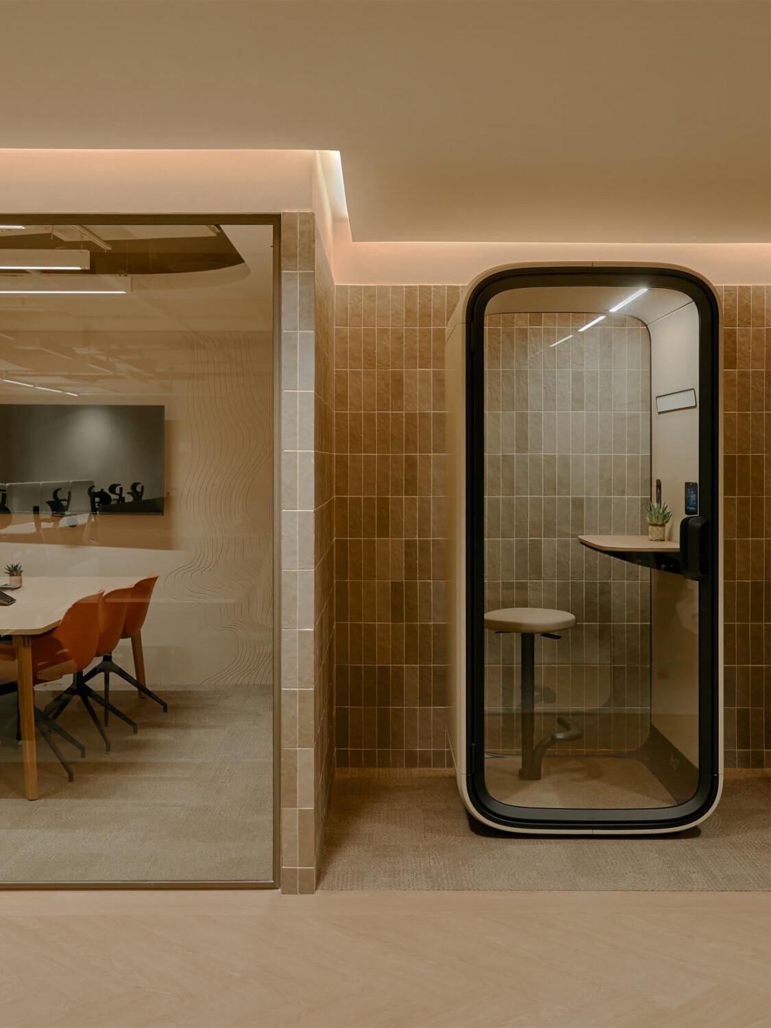 A sand toned office phone booth next to a meeting room.