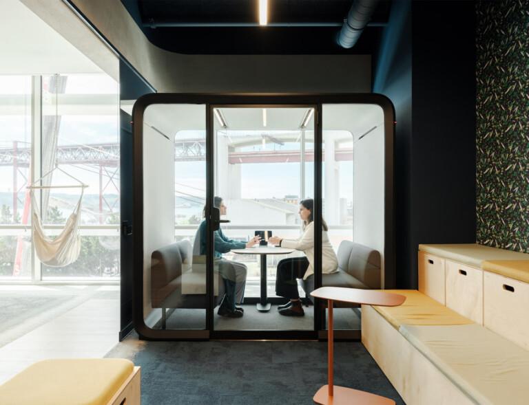 Two people sitting inside a Framery Four meeting pod at an office.