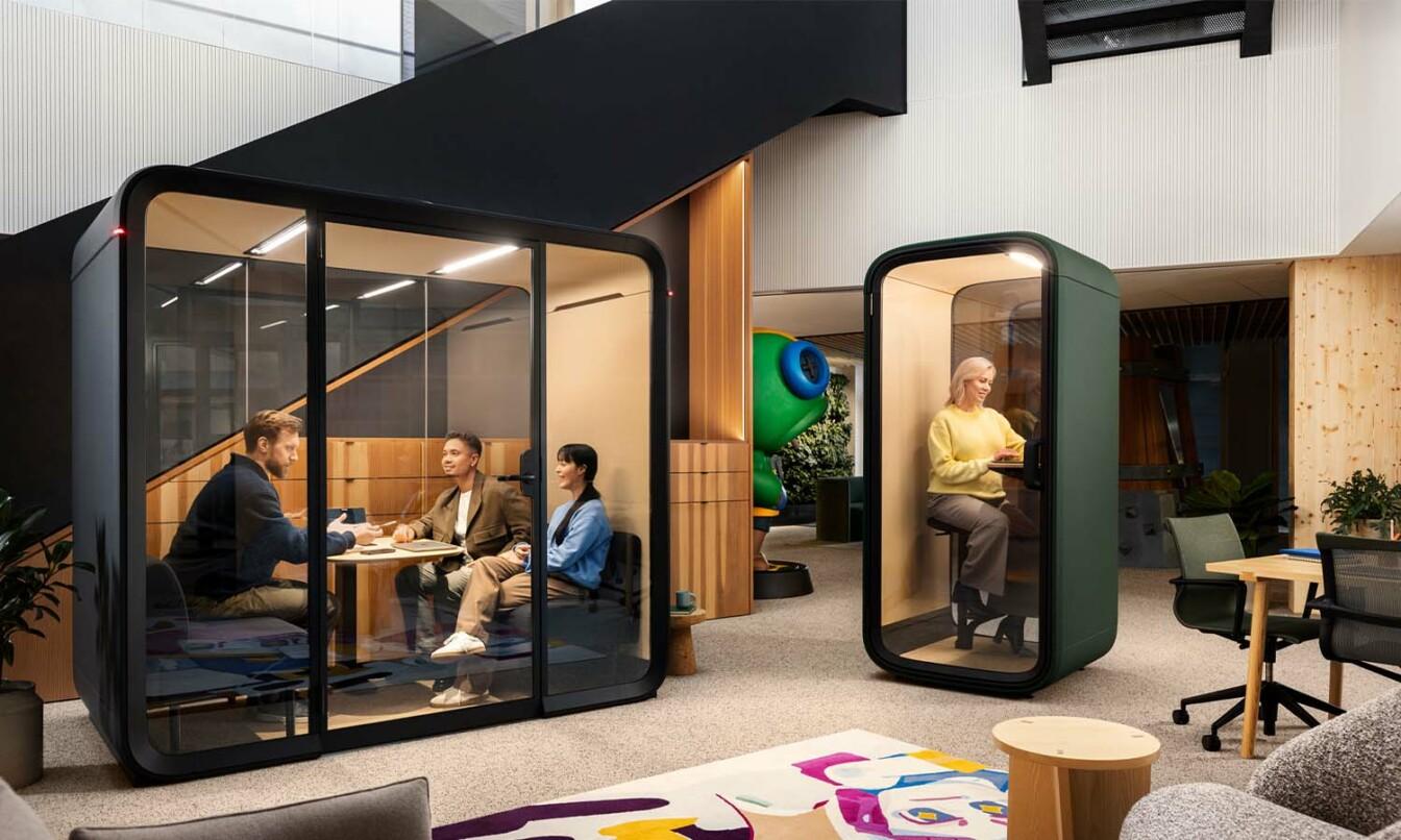 Framery Four meeting pod and Framery One Compact smart pod in a multifunctional office space with colorful and modern decor and people having meetings inside the pods.