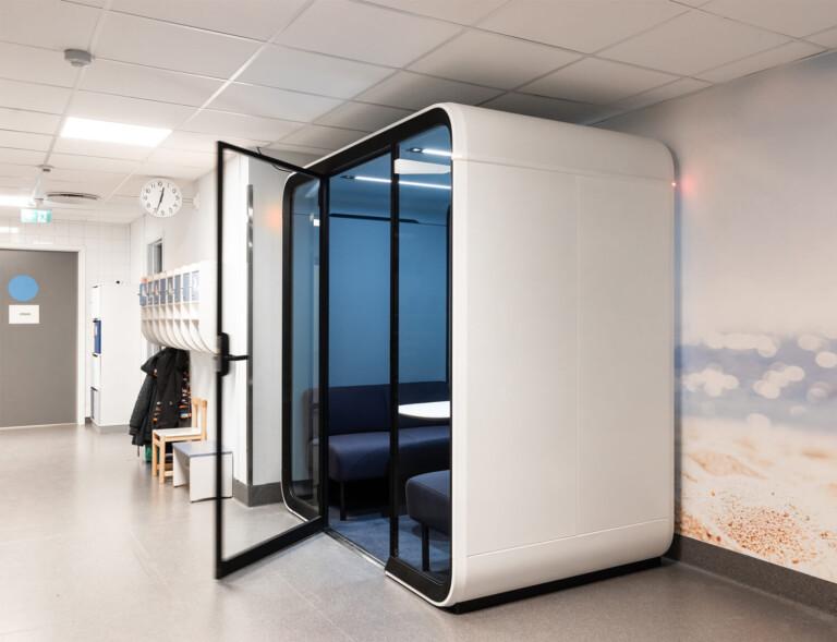A light colored empty school hallway with a whit a study pod.